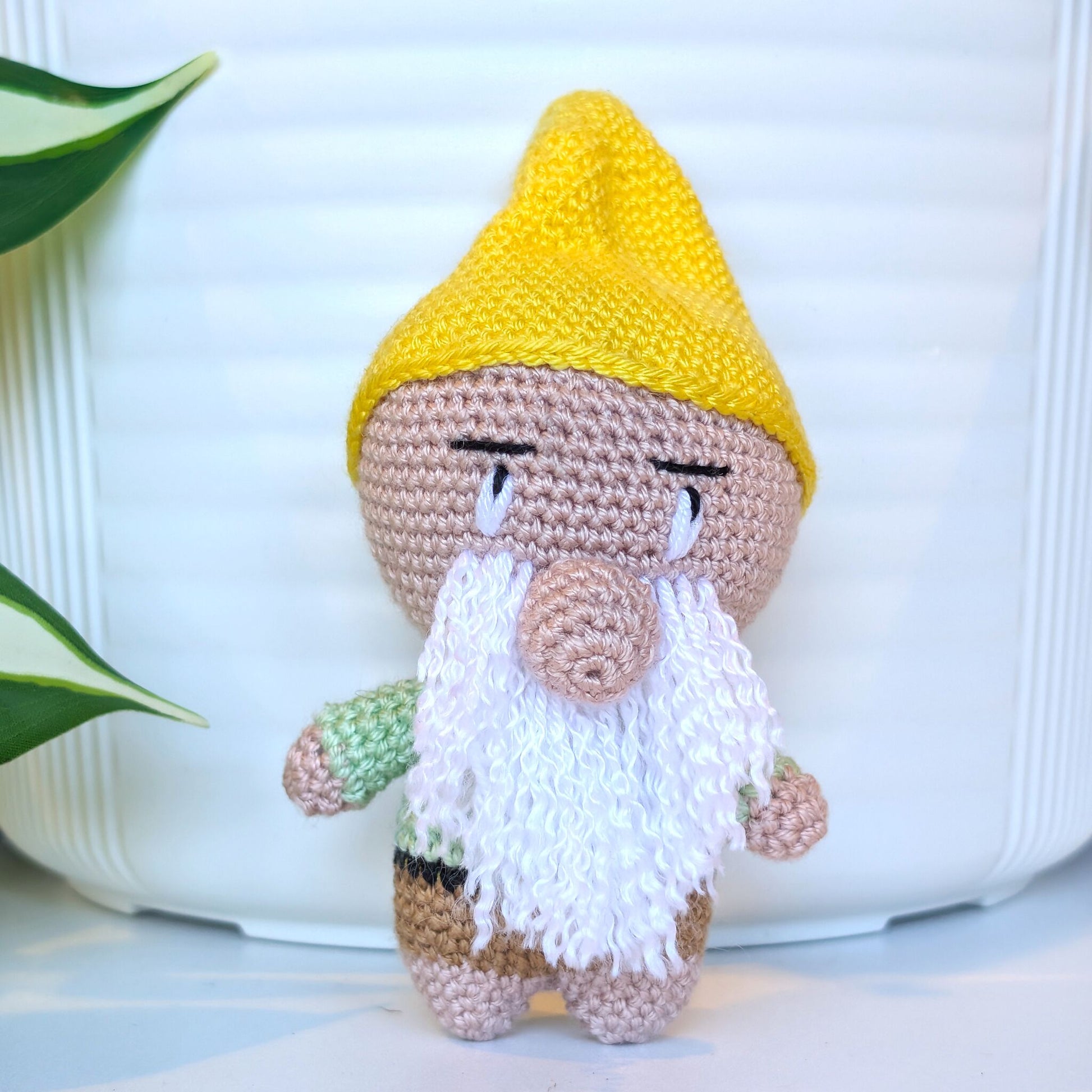Crocheted plush gnome toy with a yellow hat and white beard on a light background