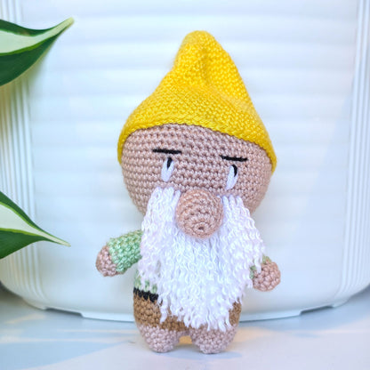 Crocheted plush gnome toy with a yellow hat and white beard on a light background