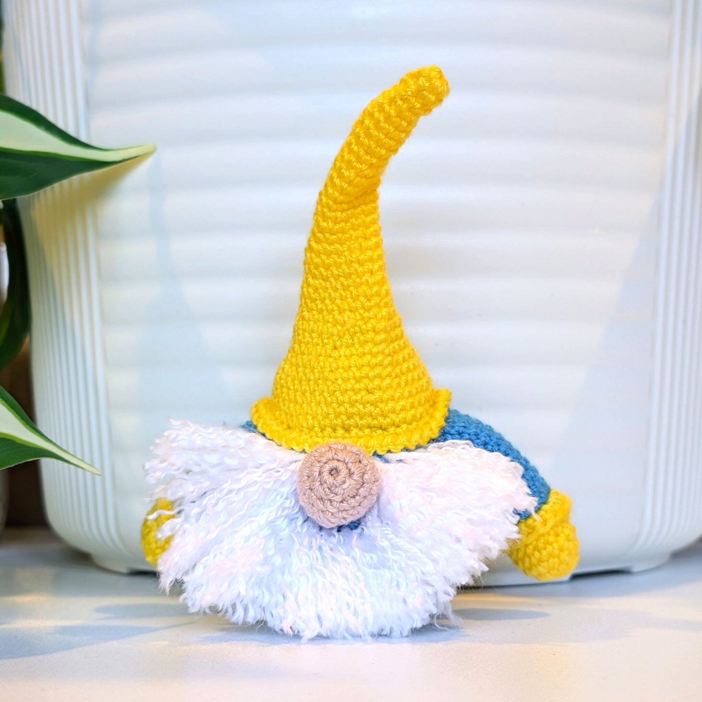 Handmade crochet Scandinavian gnome with a sunflower yellow hat, azure blue shirt, and white beard 