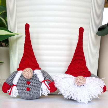 Crocheted Nordic gnomes with red hats and gray bodies on a white surface.