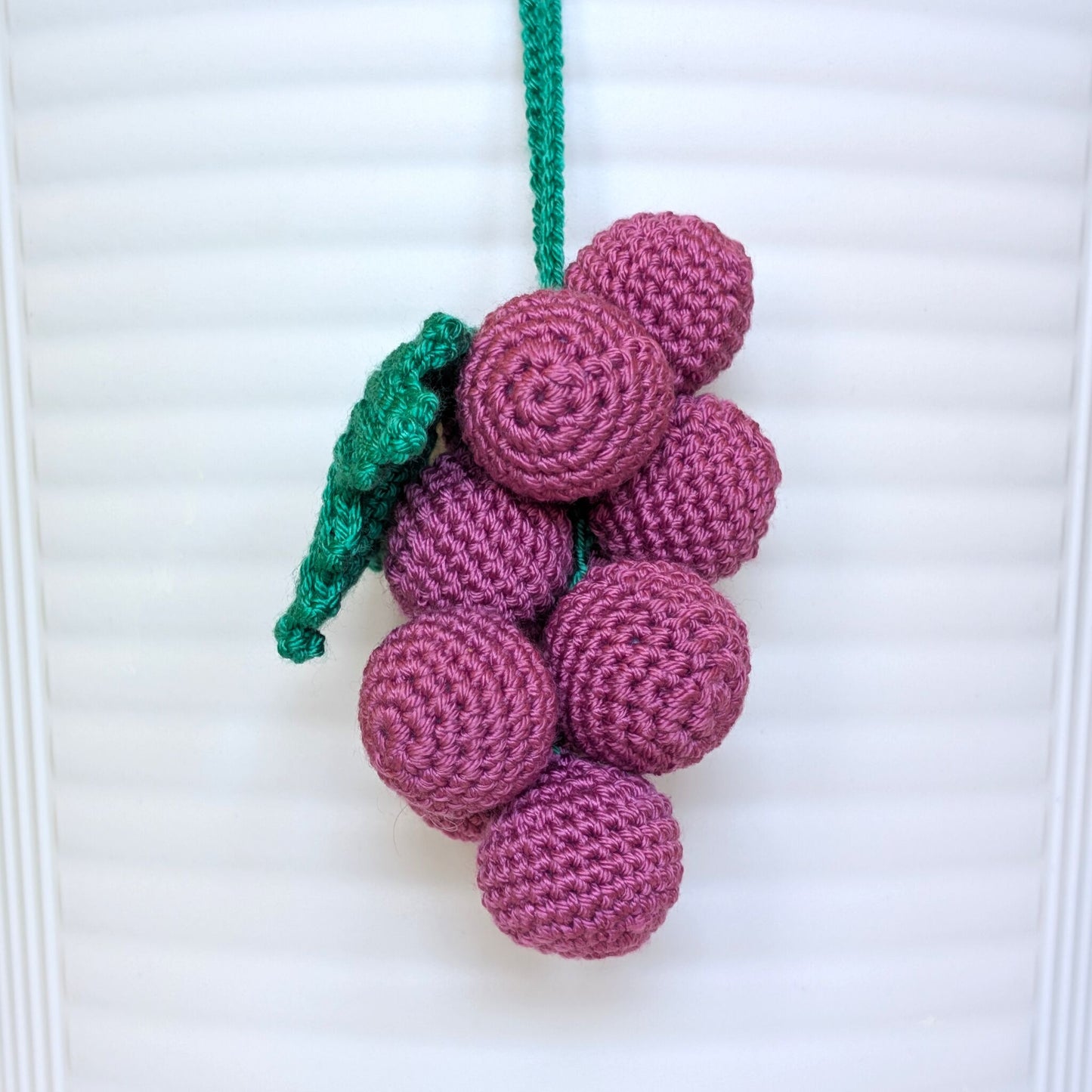 Crocheted pastel burgundy grapes with a green stem and string