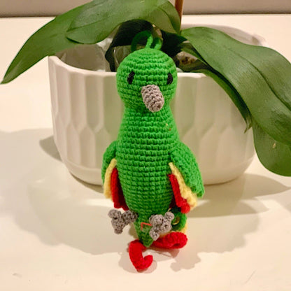 Crocheted green parrot with multi-colored tail feathers and wings on white surface