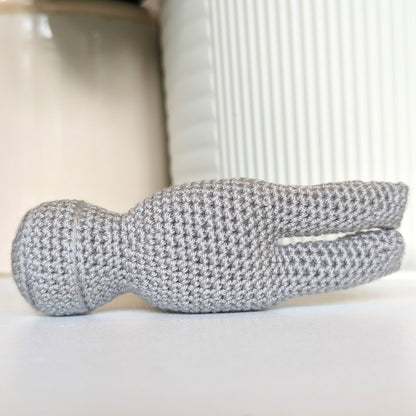 A crocheted hammer with a light gray head in front of a white ribbed cylindrical planter pot.