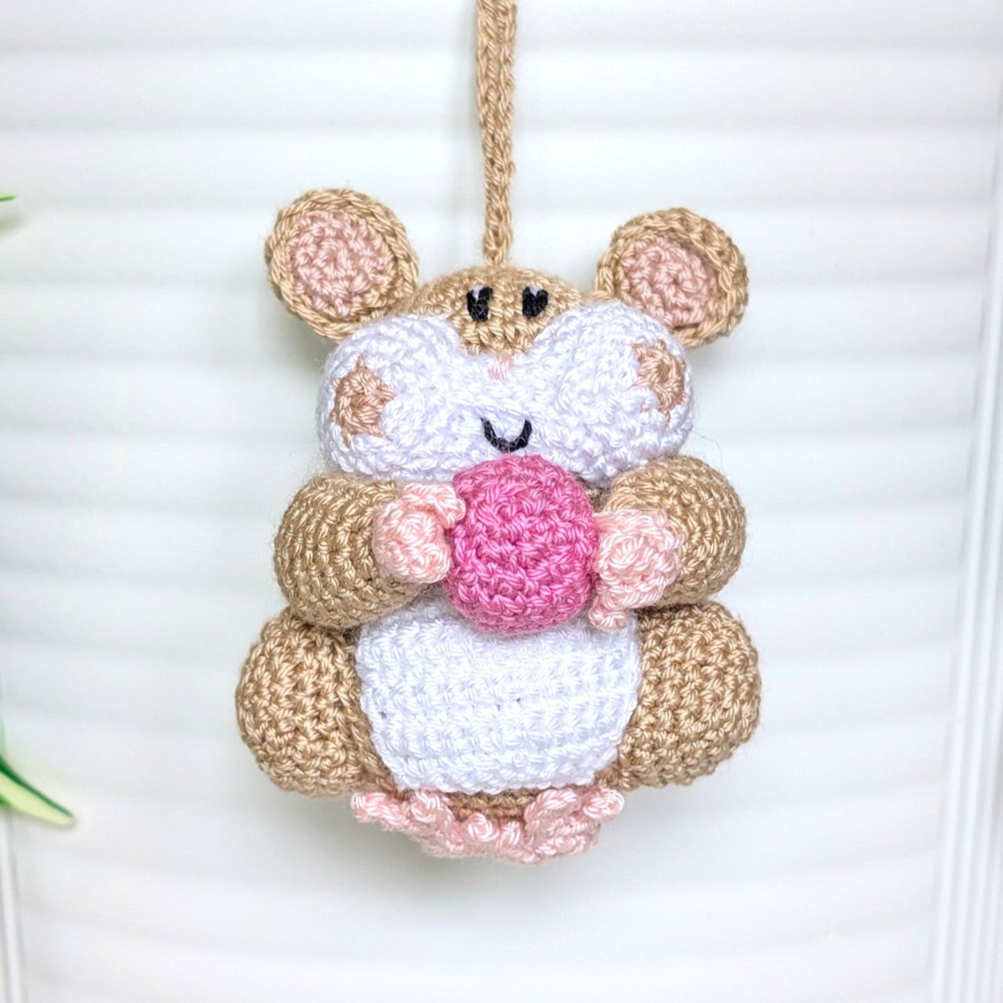 Crocheted beige hamster charm attached to a string, holding an orchid pink colored ball