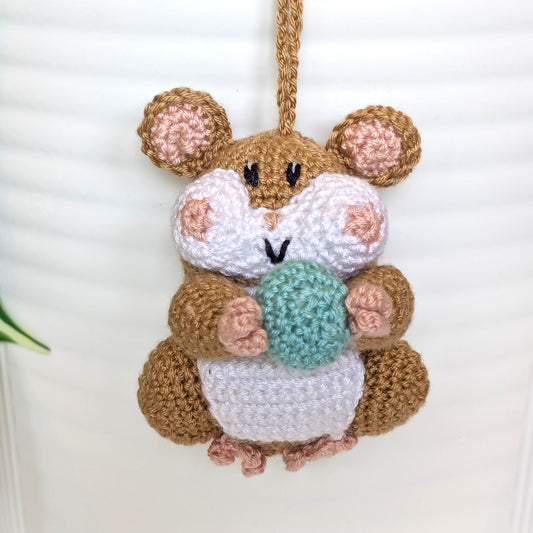 Crochet sand brown hamster bag charm with a string holding an aqua colored ball
