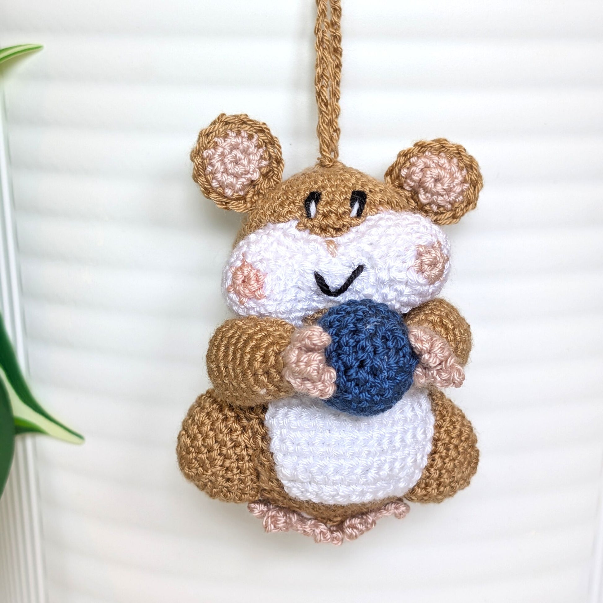 Crochet sand brown hamster bag charm with a string holding a dark blue ball