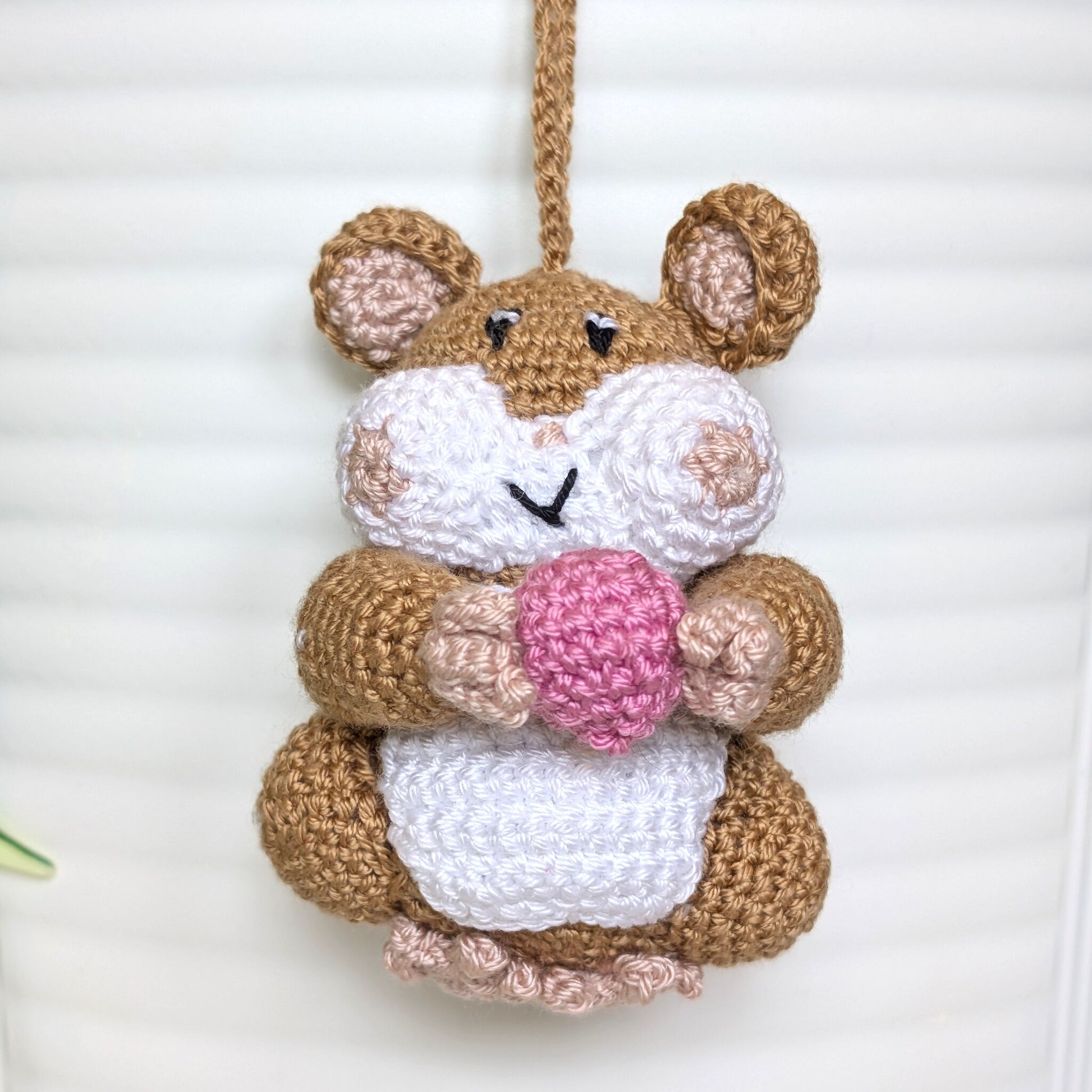 Crochet sand brown hamster bag charm with a string holding a french pink colored ball