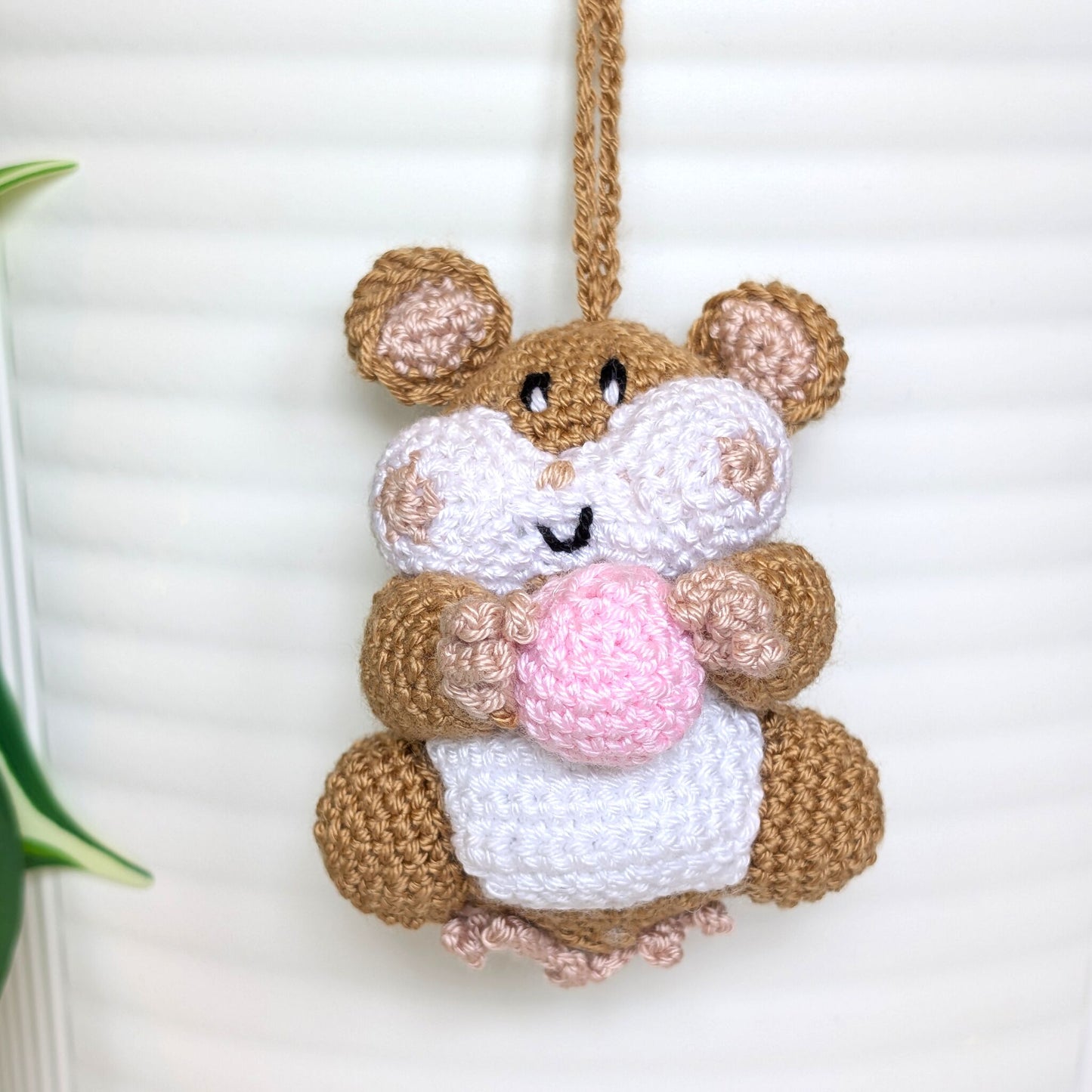 Crochet sand brown hamster bag charm with a string holding a light pink colored ball