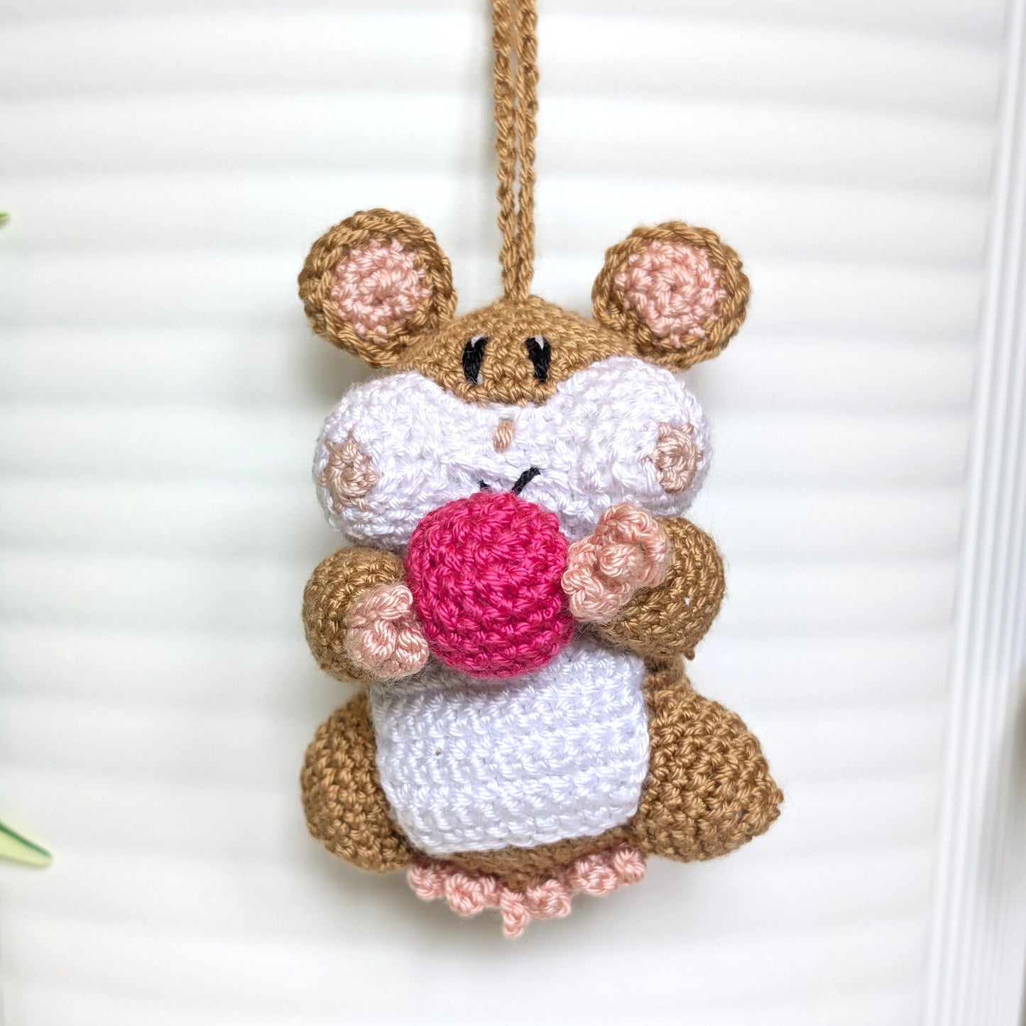 Crochet sand brown hamster bag charm with a string holding a rose colored ball