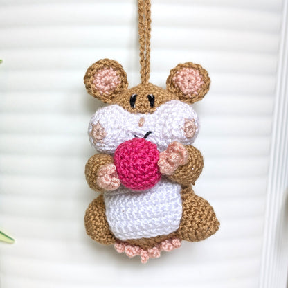 Crochet sand brown hamster bag charm with a string holding a rose colored ball