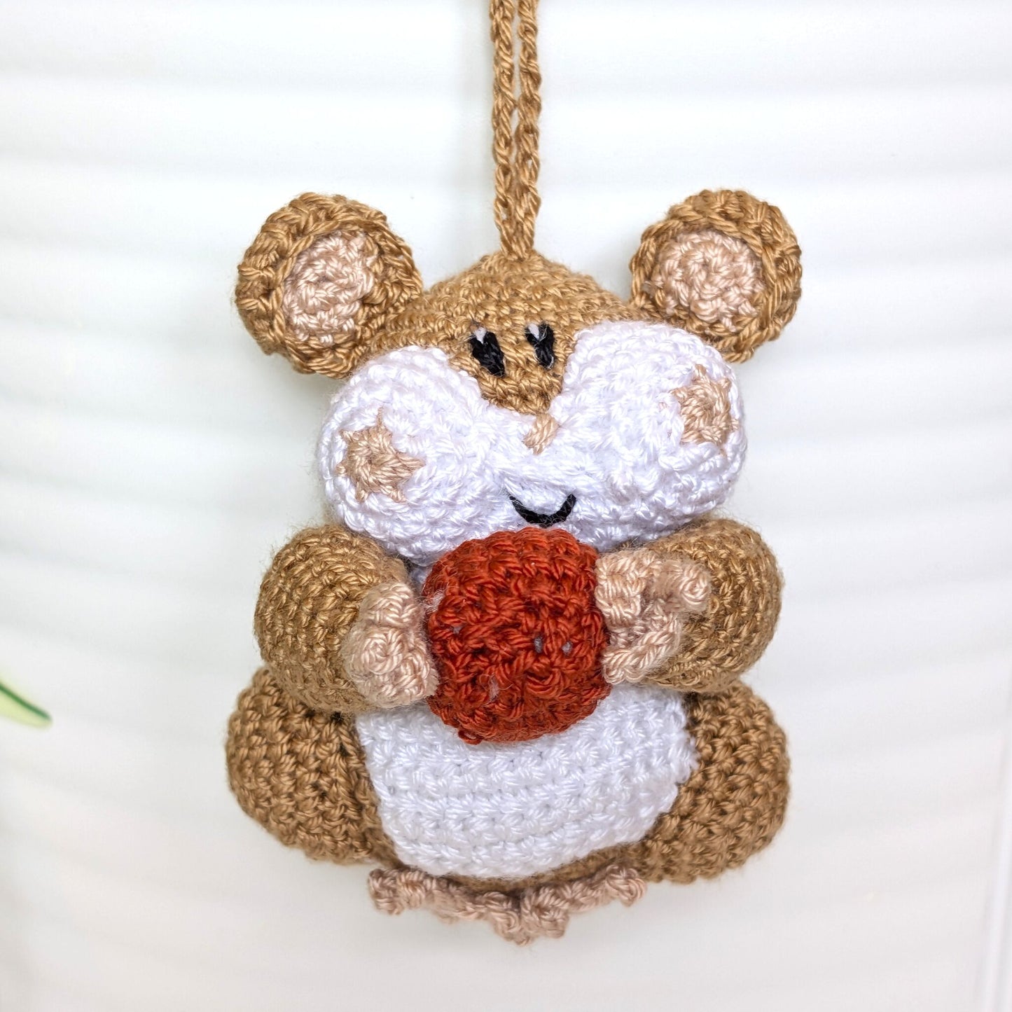 Crochet sand brown hamster bag charm with a string holding an terracotta colored ball