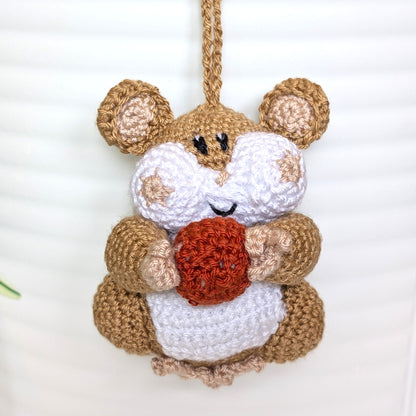Crochet sand brown hamster bag charm with a string holding an terracotta colored ball