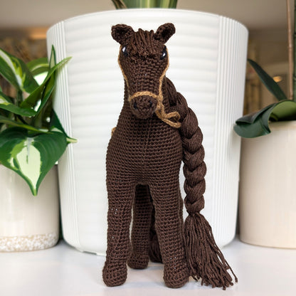Front view of crocheted horse plush with braided mane and tail with beige saddle