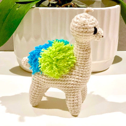 Crocheted llama toy with a blue and green accents on a white surface.