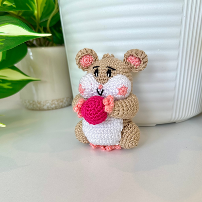Crocheted beige hamster charm attached to a string, holding a rose pink ball