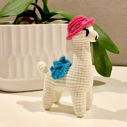 Crocheted plush llama toy with a pink hat and azure blue saddle.