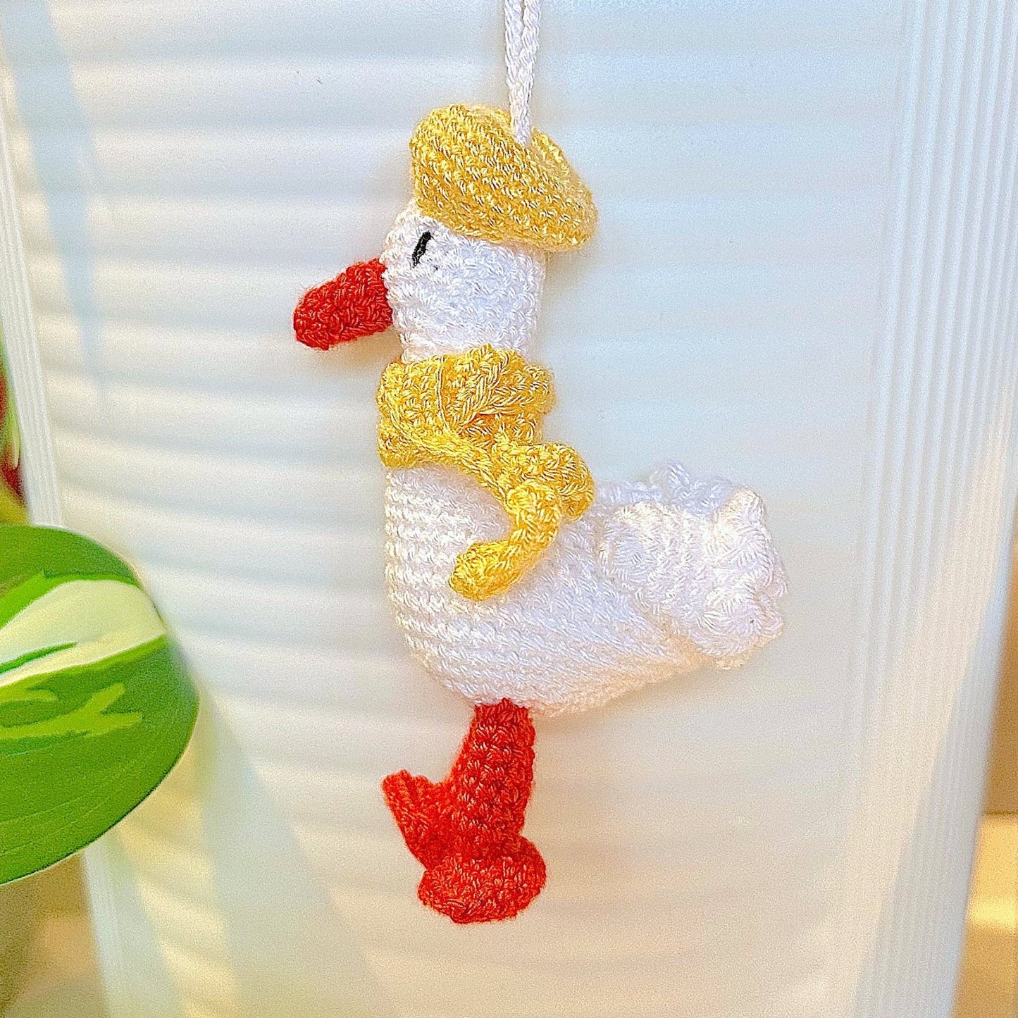 Crocheted duck keychain charm wearing a light yellow beret and scarf, attached to a string
