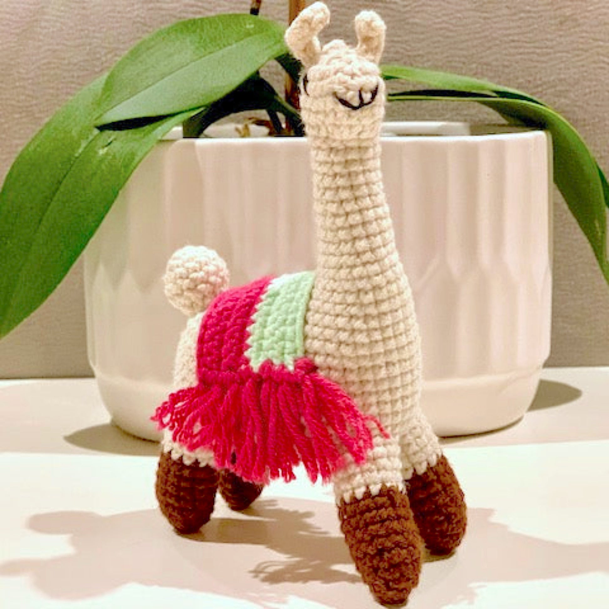 Crocheted llama toy with fringed saddle in hot pink and pastel mint colors