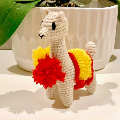 Crocheted llama toy with red and yellow accents on a white surface.
