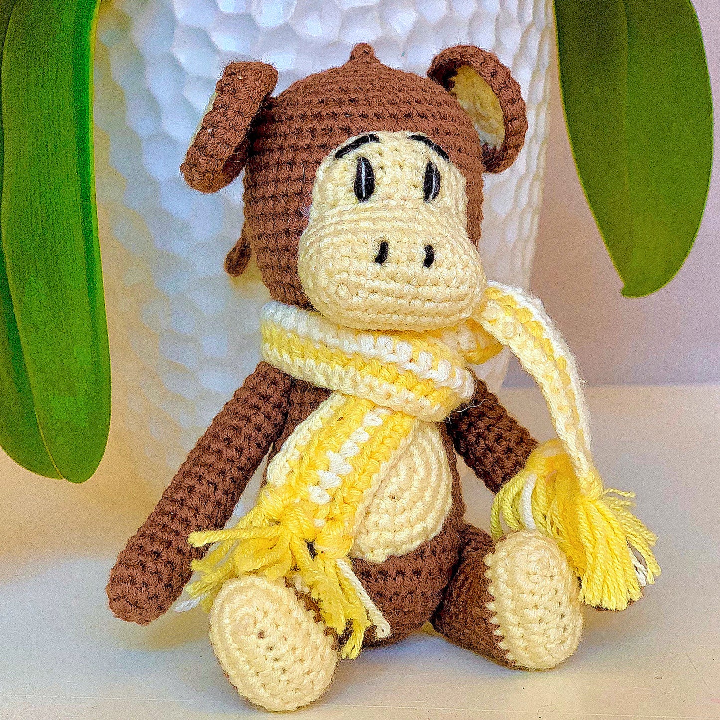 Crocheted plush monkey toy with a yellow scarf on a light background
