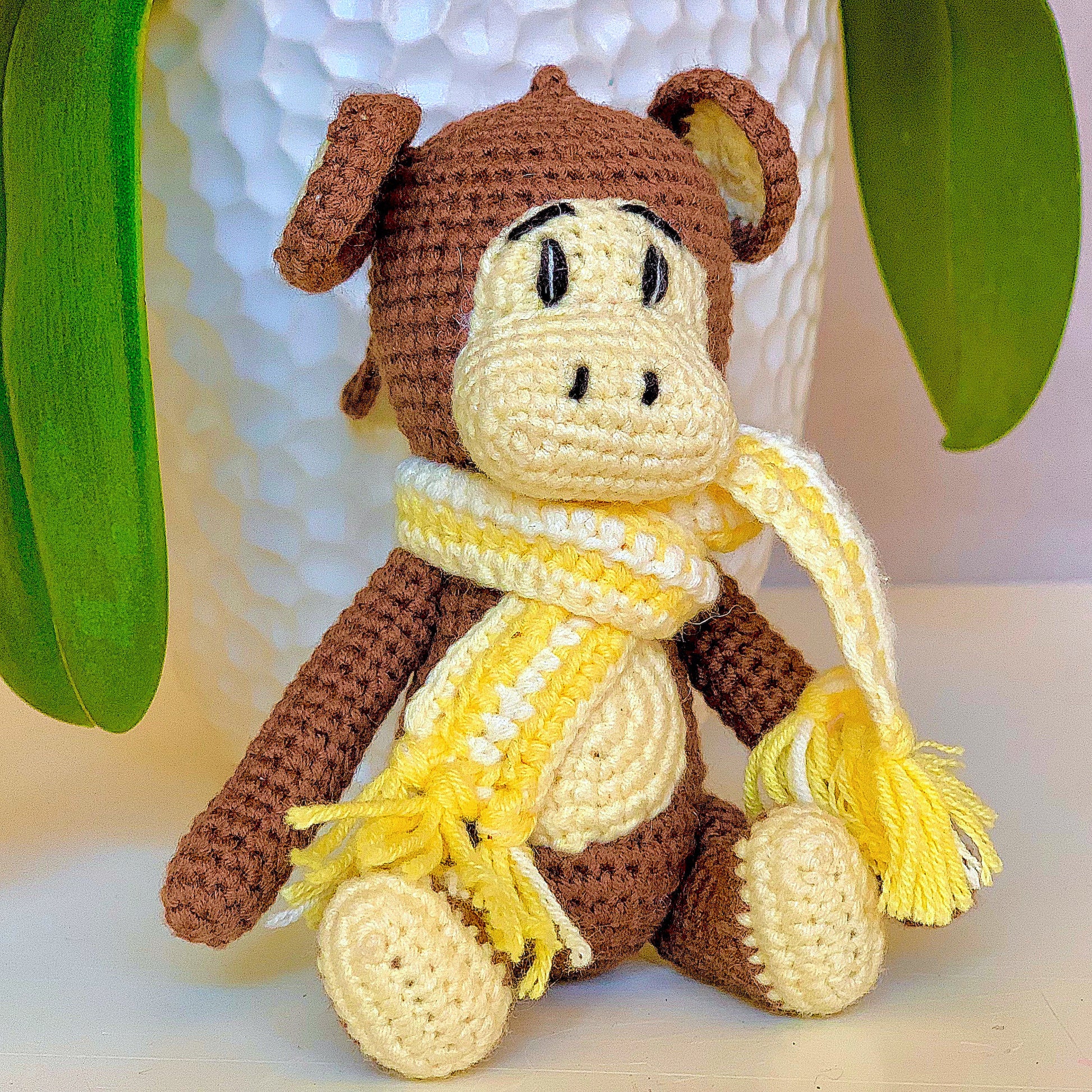 Crocheted plush monkey toy with a yellow scarf on a light background