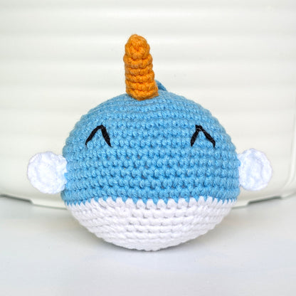 A handmade crocheted plush narwhal toy with a small orange horn 