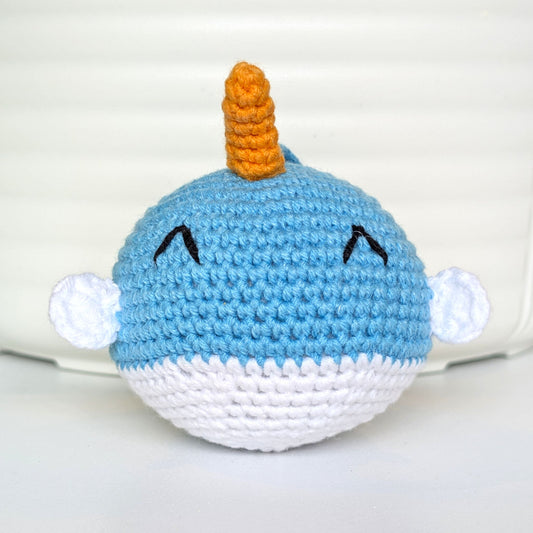 A handmade crocheted plush narwhal toy with a small orange horn 