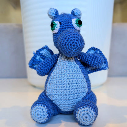 Refugee-made blue crocheted hippo toy sitting on a surface with a white cup in the background.