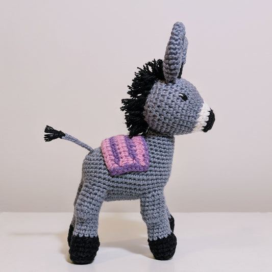 Crocheted plush donkey toy with a pink and lavender striped saddle