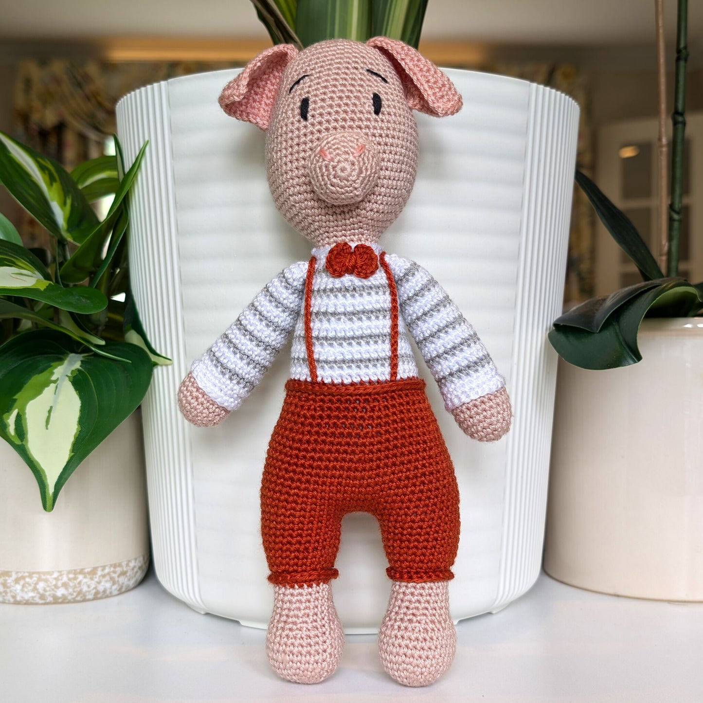 Crocheted standing pig wearing a striped terracotta sweater, gray pants and a bow tie