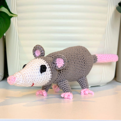 Crocheted opossum toy on a light surface with a neutral background