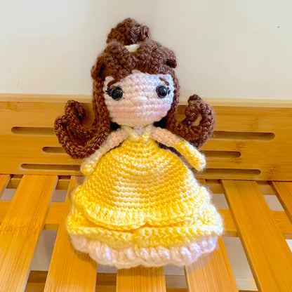Crocheted princess doll with brown hair and a yellow dress on a wooden surface