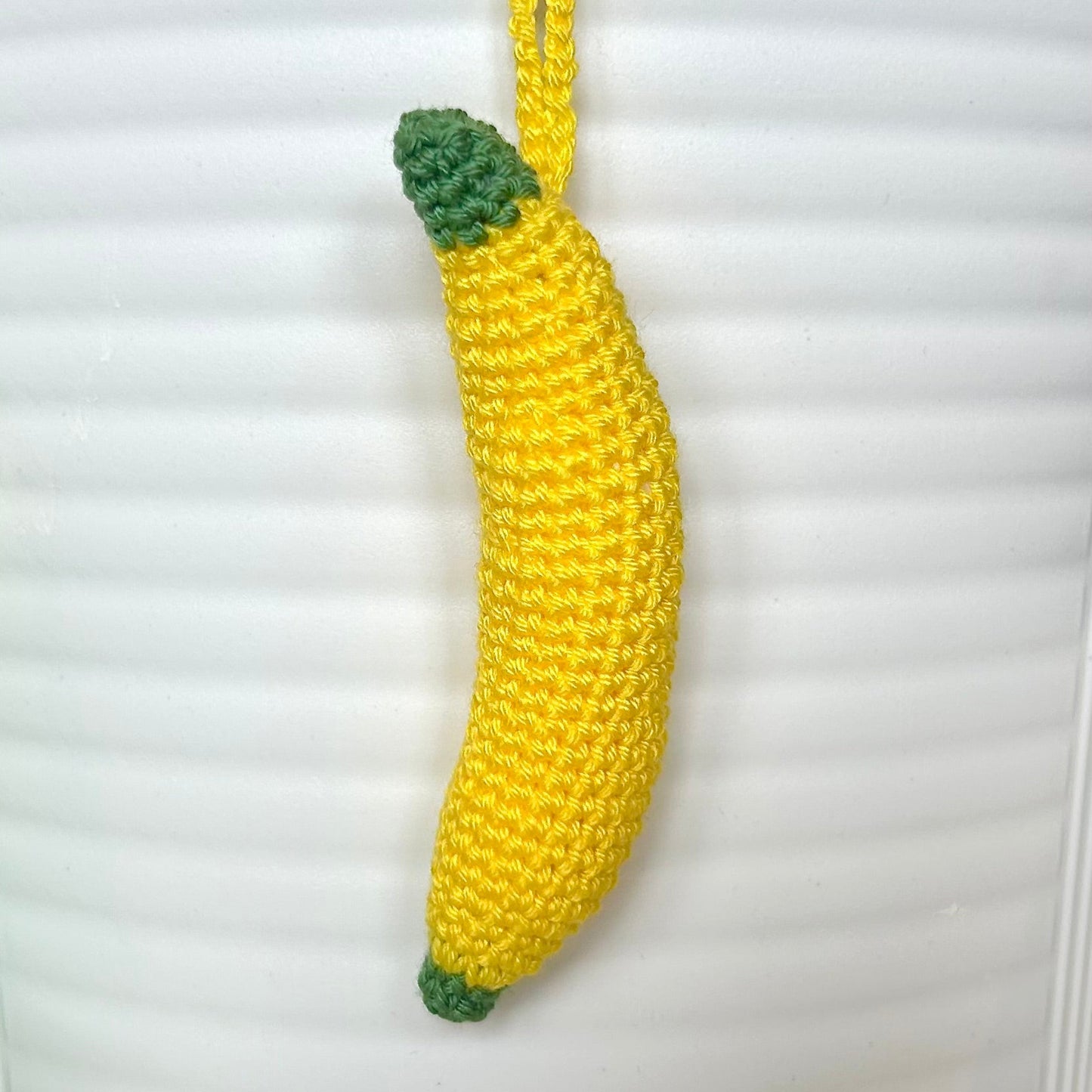 Crocheted yellow banana charm with a green stem