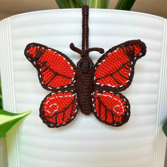Mini crocheted butterfly charm in red-orange and brown colors. 