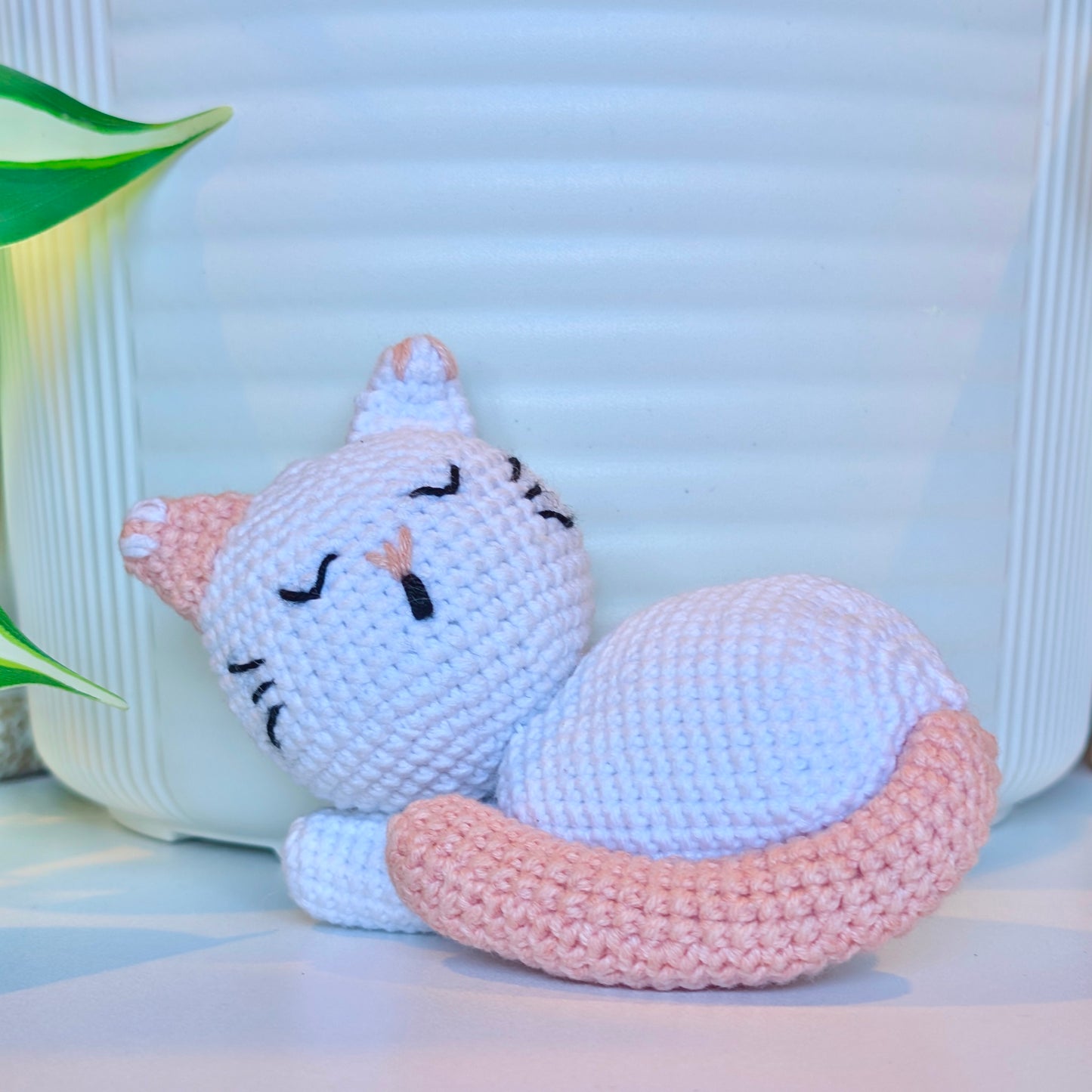Crocheted white sleeping cat with a light coral tail, ears, and nose