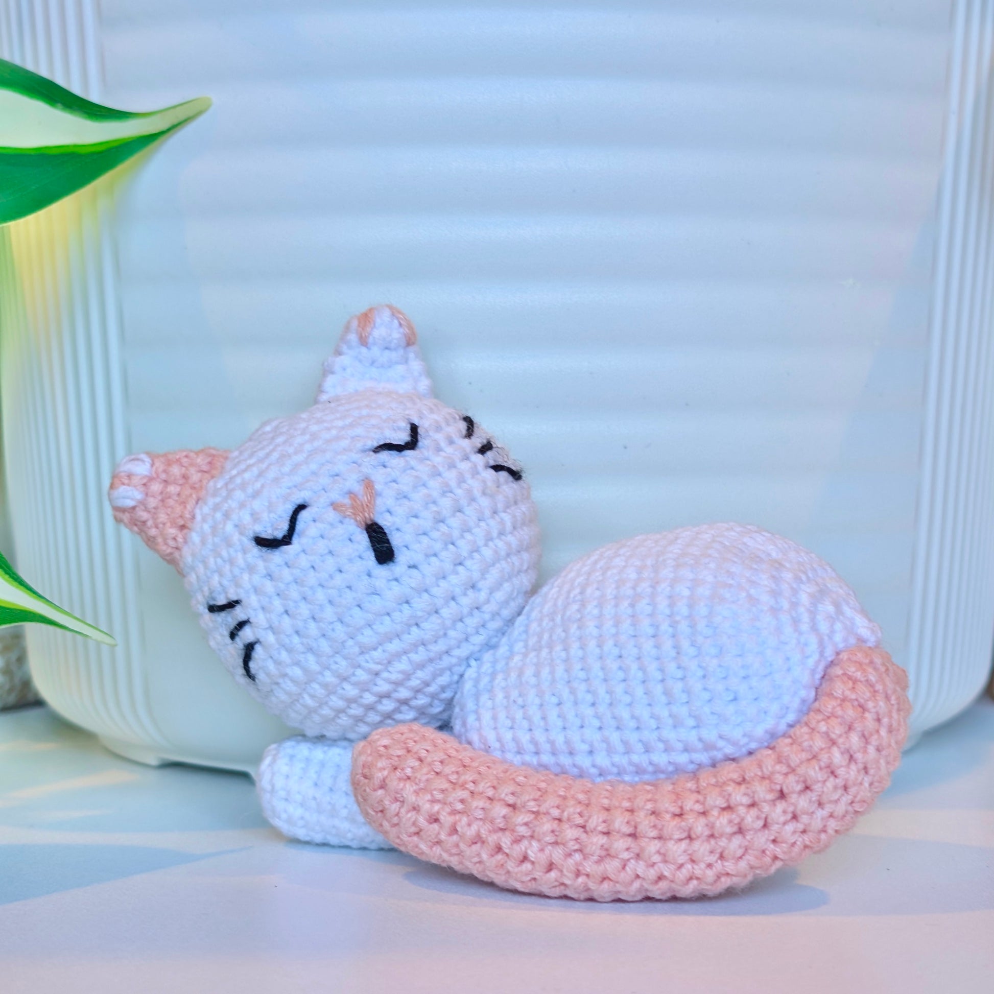 Crocheted white sleeping cat with a light coral tail, ears, and nose