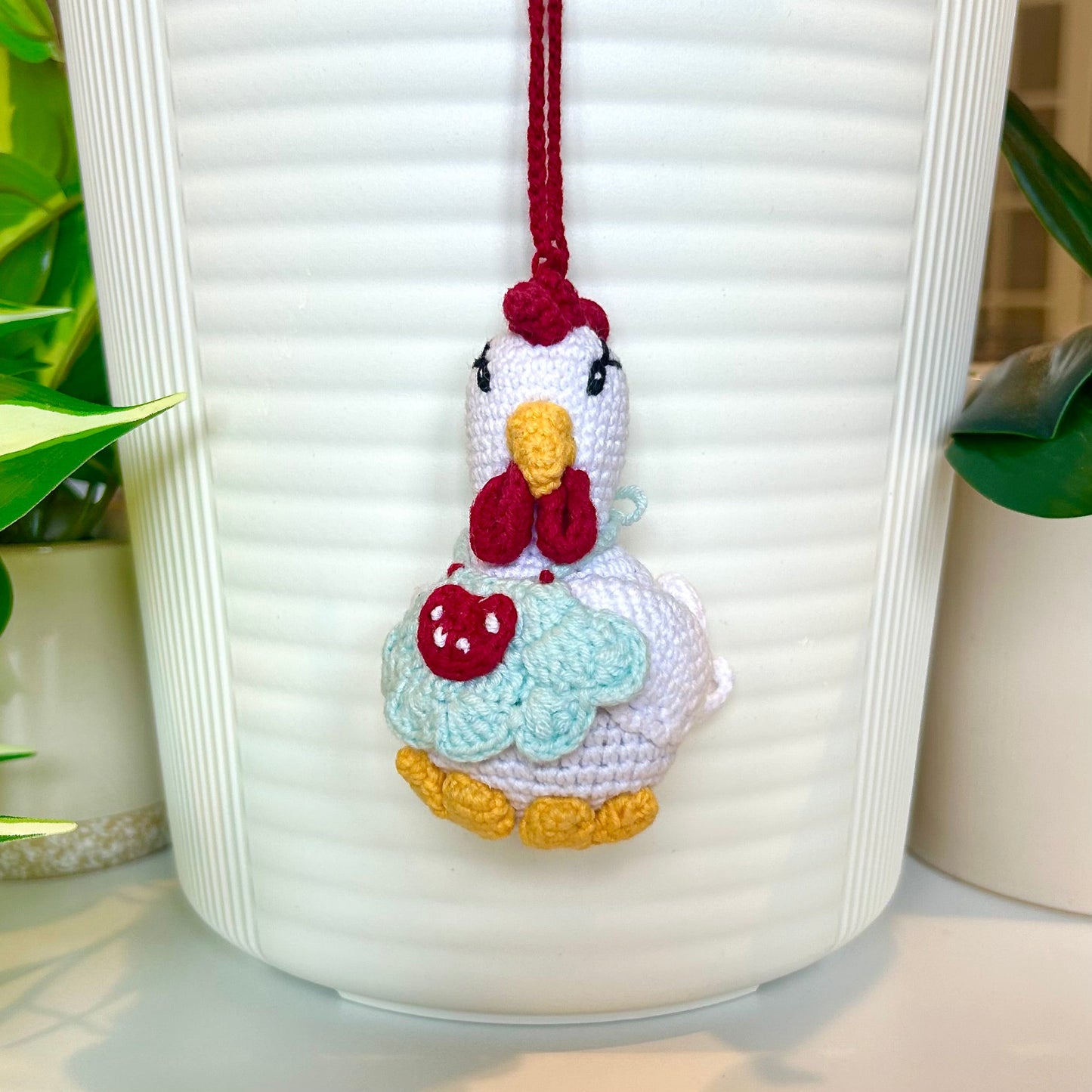 white crocheted chicken charm wearing a pale blue apron with red and white accents