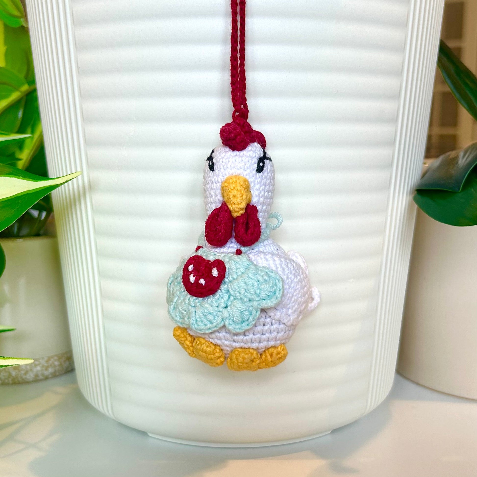 white crocheted chicken charm wearing a pale blue apron with red and white accents