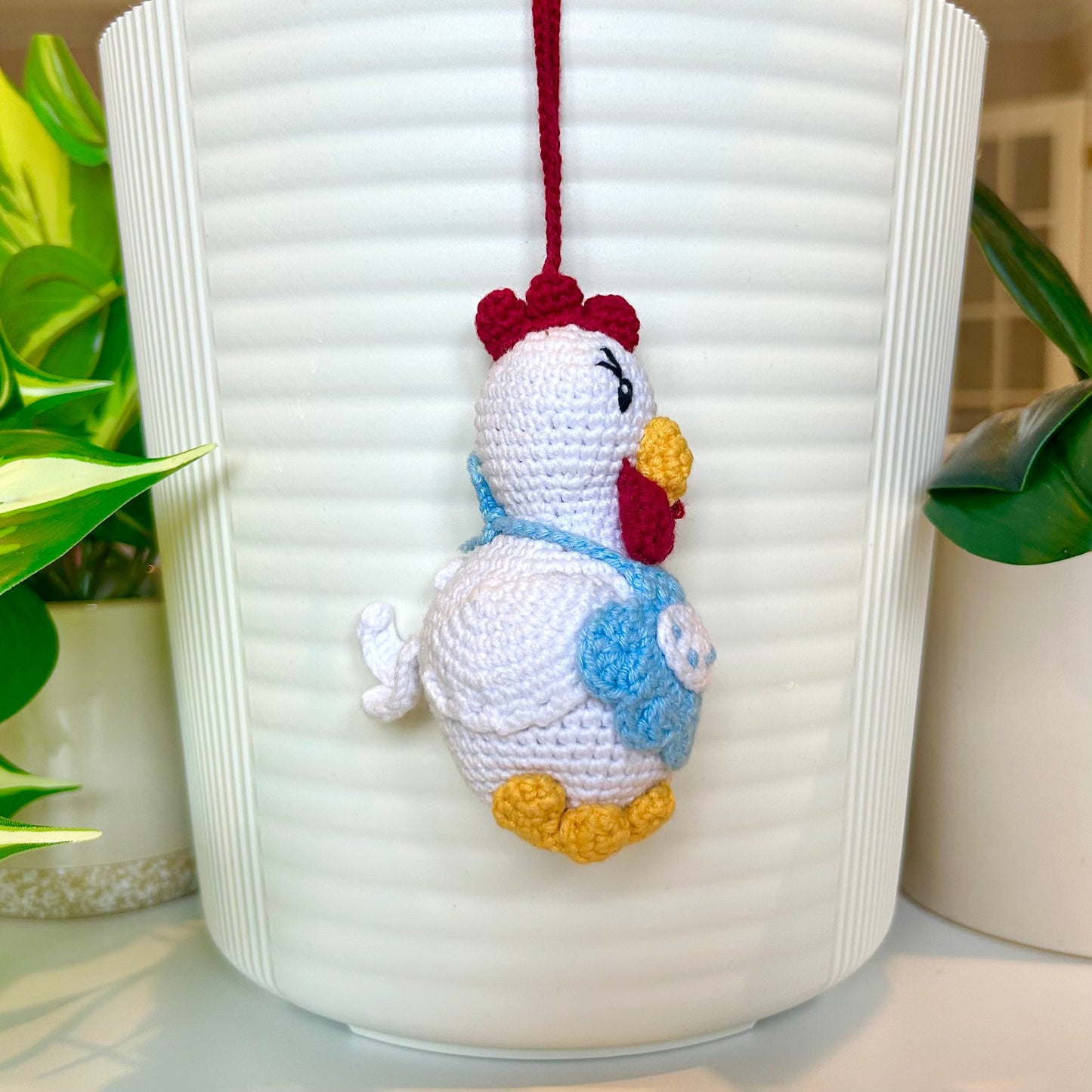 Right side profile of crocheted chicken charm wearing a sky blue apron 