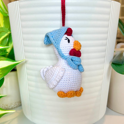 white crocheted chicken charm with eyelashes, red comb, and a sky blue kerchief