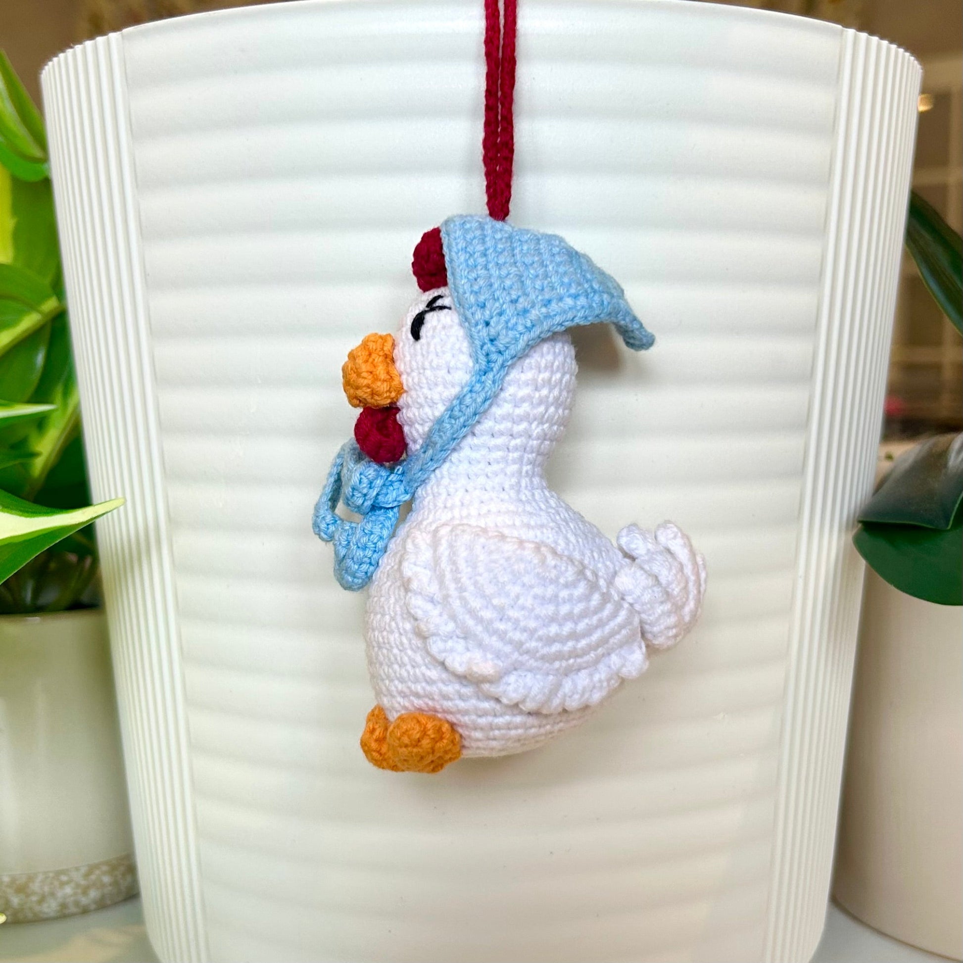 Right side profile of white crocheted chicken charm with red comb and a sky blue kerchief