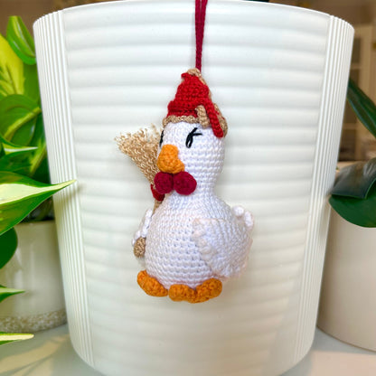 White crocheted chicken charm wearing a red and tan hat and carrying a broom