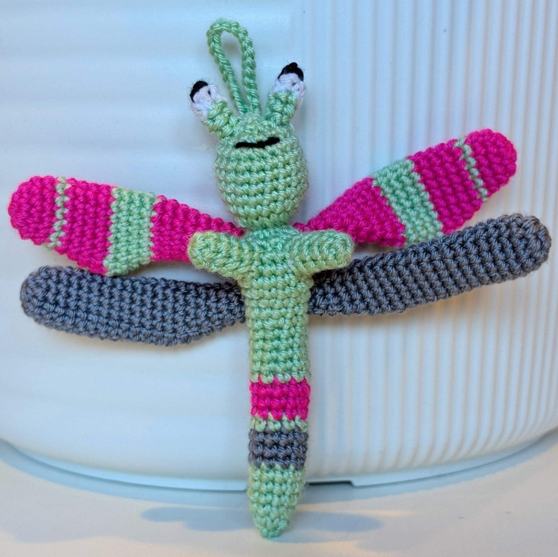 Crocheted dragonfly charm with mint green, hot pink, and gray stripes