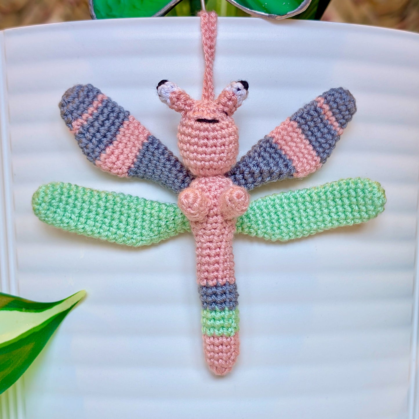 Small crocheted dragonfly bag charm with pink, gray, and mint green stripes
