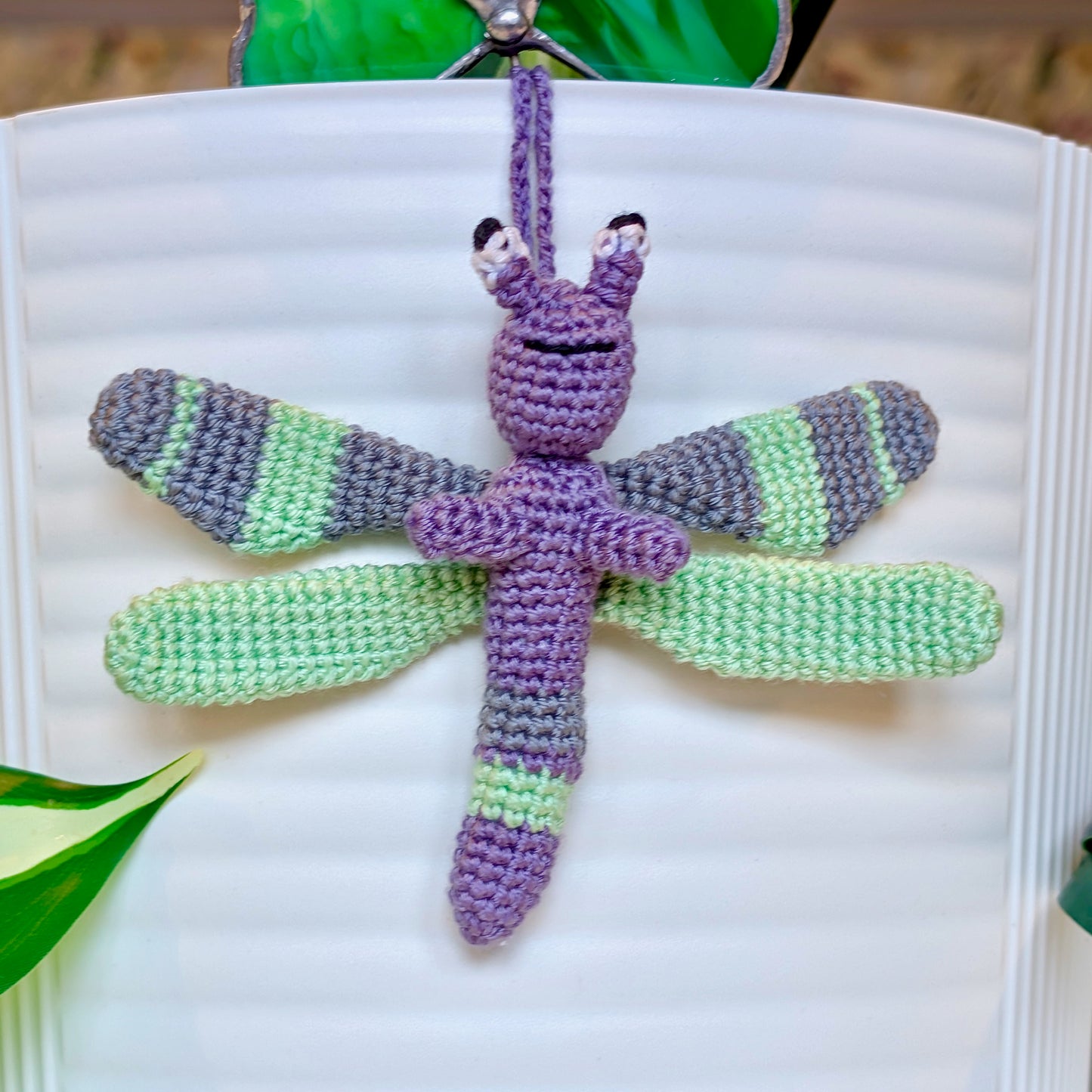 Small crocheted dragonfly bag charm with purple, mint green, and gray stripes