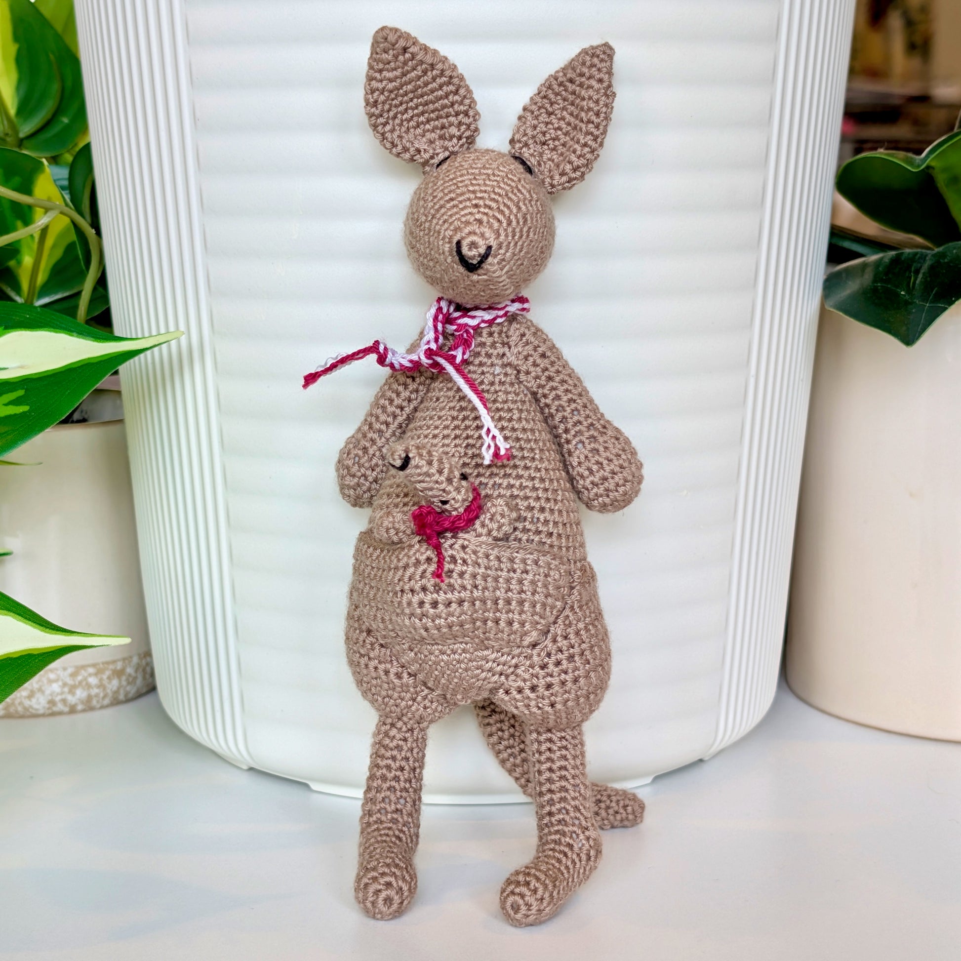 Crocheted kangaroo wearing a berry and white scarf with a baby joey in her pouch wearing a berry scarf