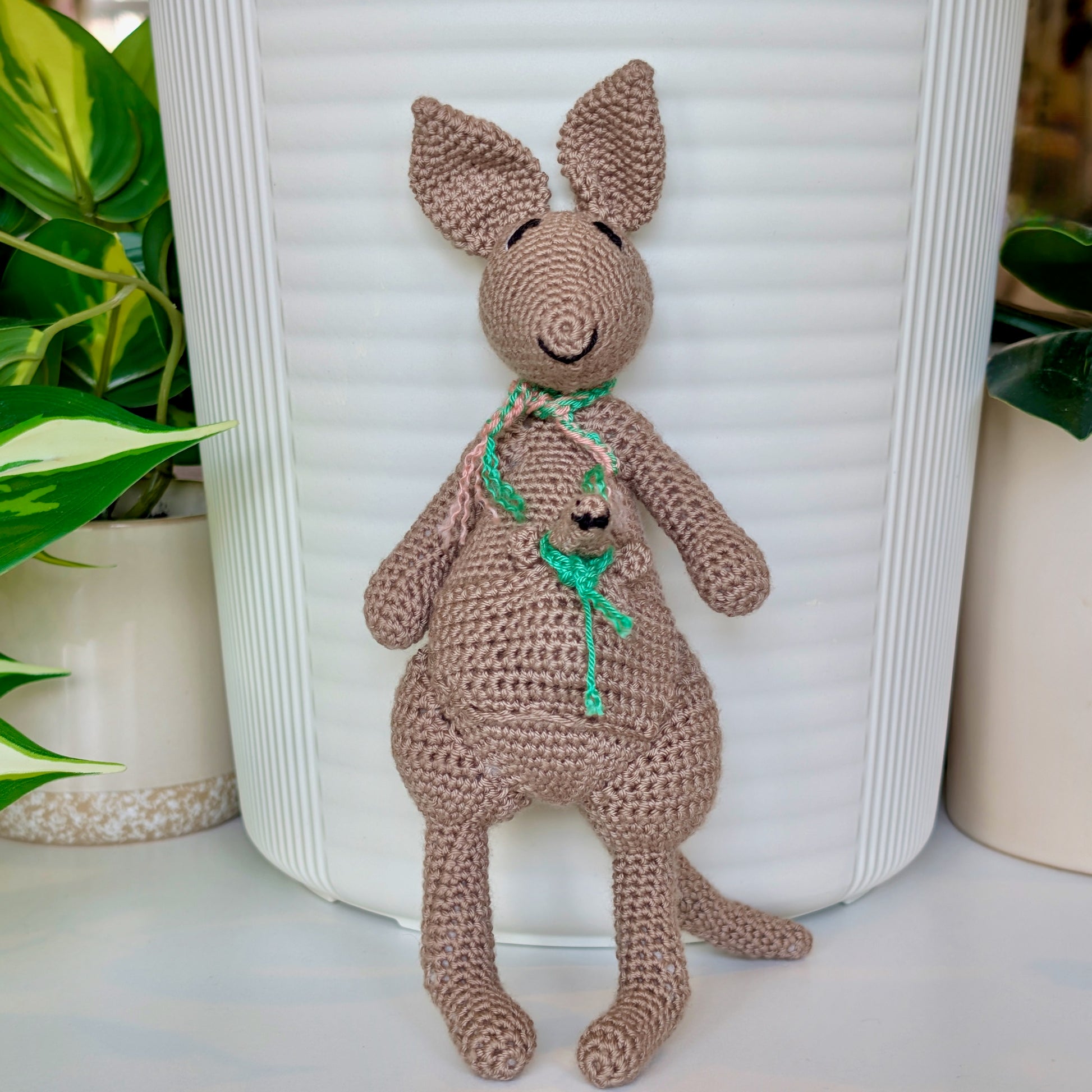 Crocheted kangaroo wearing an emerald green and melon pink scarf with a baby joey in her pouch also wearing an emerald scarf