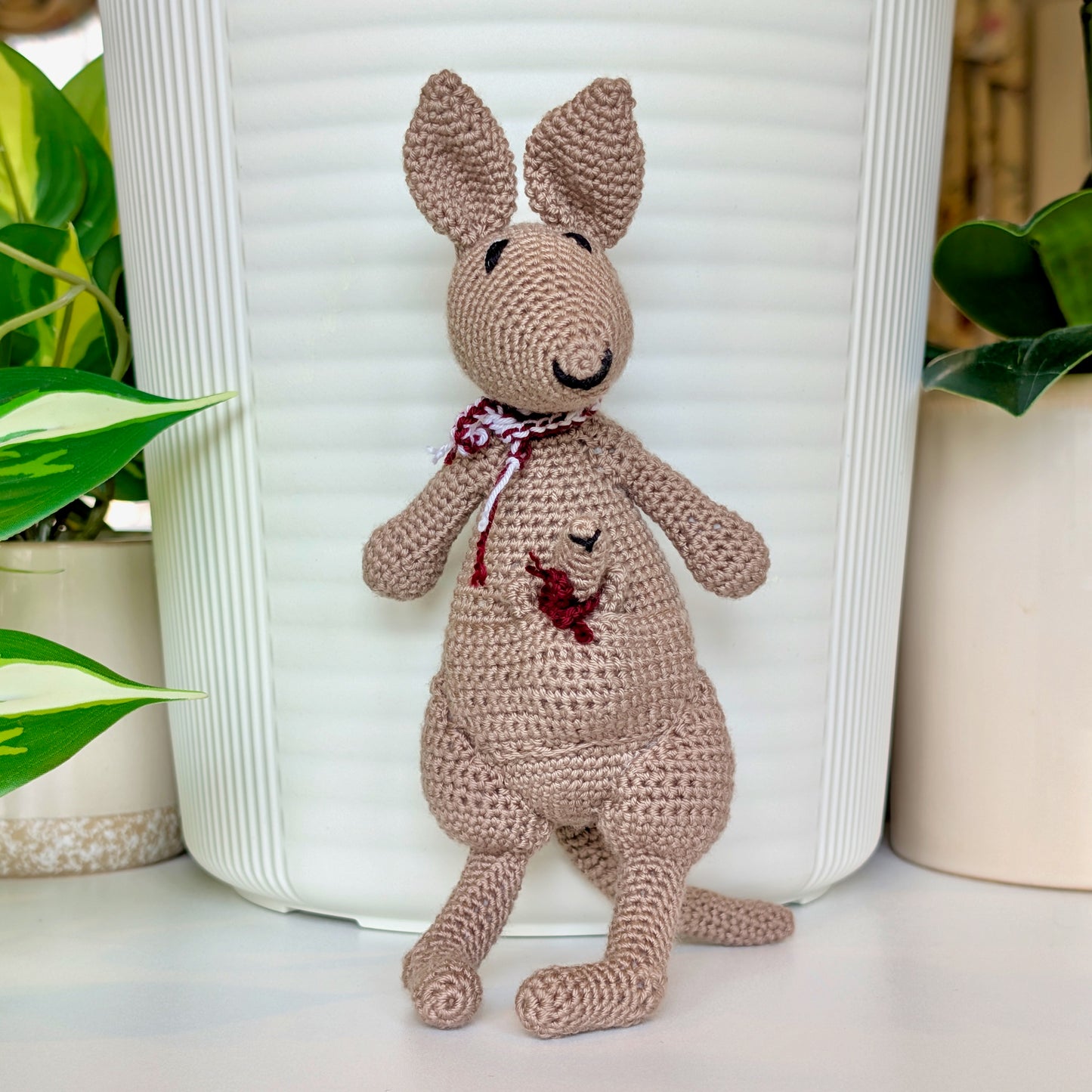 Crocheted kangaroo wearing a maroon and white scarf with a baby joey in her pouch wearing a maroon scarf