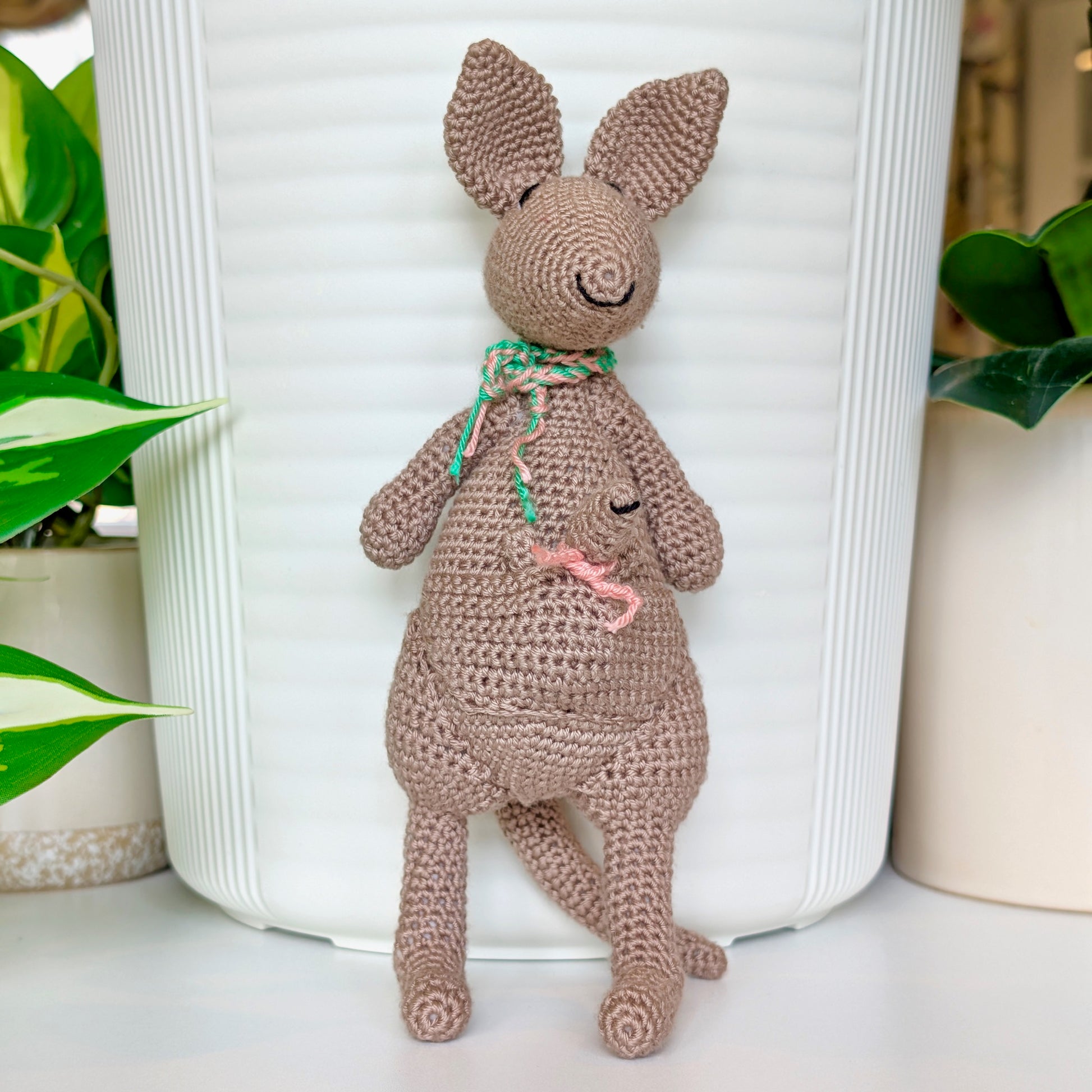Crocheted kangaroo wearing an emerald and melon pink scarf with a baby joey in her pouch wearing a melon pink scarf