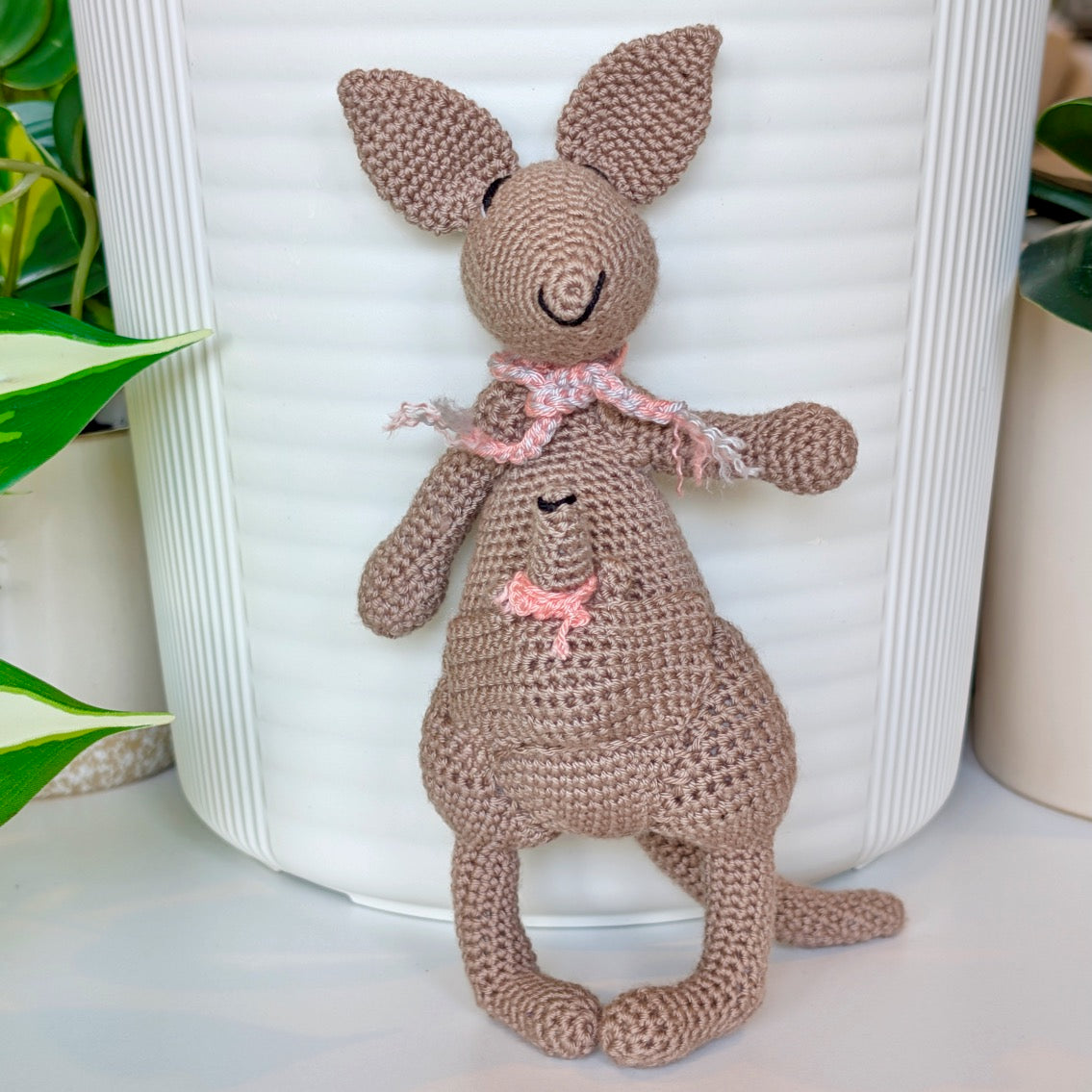 Crocheted kangaroo wearing a melon pink and gray scarf with a baby joey in her pouch also wearing a melon scarf